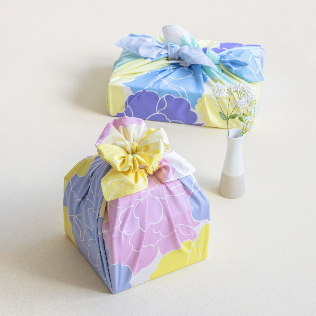 photo d'ambiance d'un emballage cadeau réalisé avec le furoshiki au motif de pivoines dans les tons jaune acidulé, bleus, vert d'eau, violets adeline x musubi en 100cm par 100cm