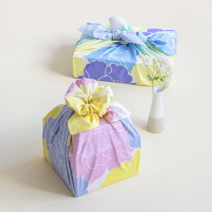 photo d'ambiance d'un emballage cadeau réalisé avec le furoshiki au motif de pivoines dans les tons jaune acidulé, bleus, vert d'eau, violets adeline x musubi en 100cm par 100cm