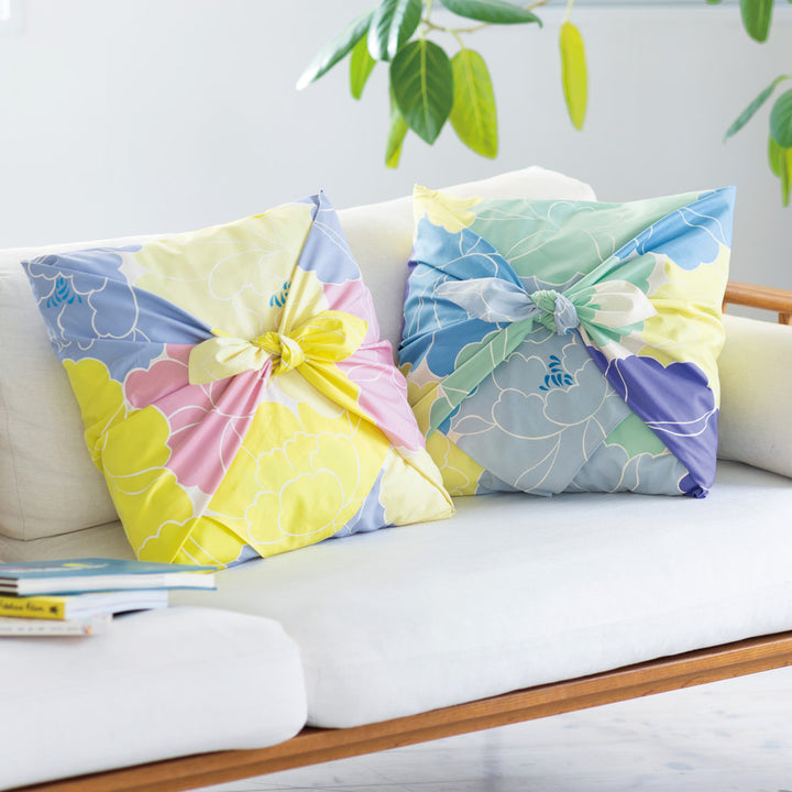 photo d'ambiance d'un coussin habillé avec le furoshiki au motif de pivoines dans les tons jaune acidulé, bleus, vert d'eau, violets adeline x musubi en 100cm par 100cm