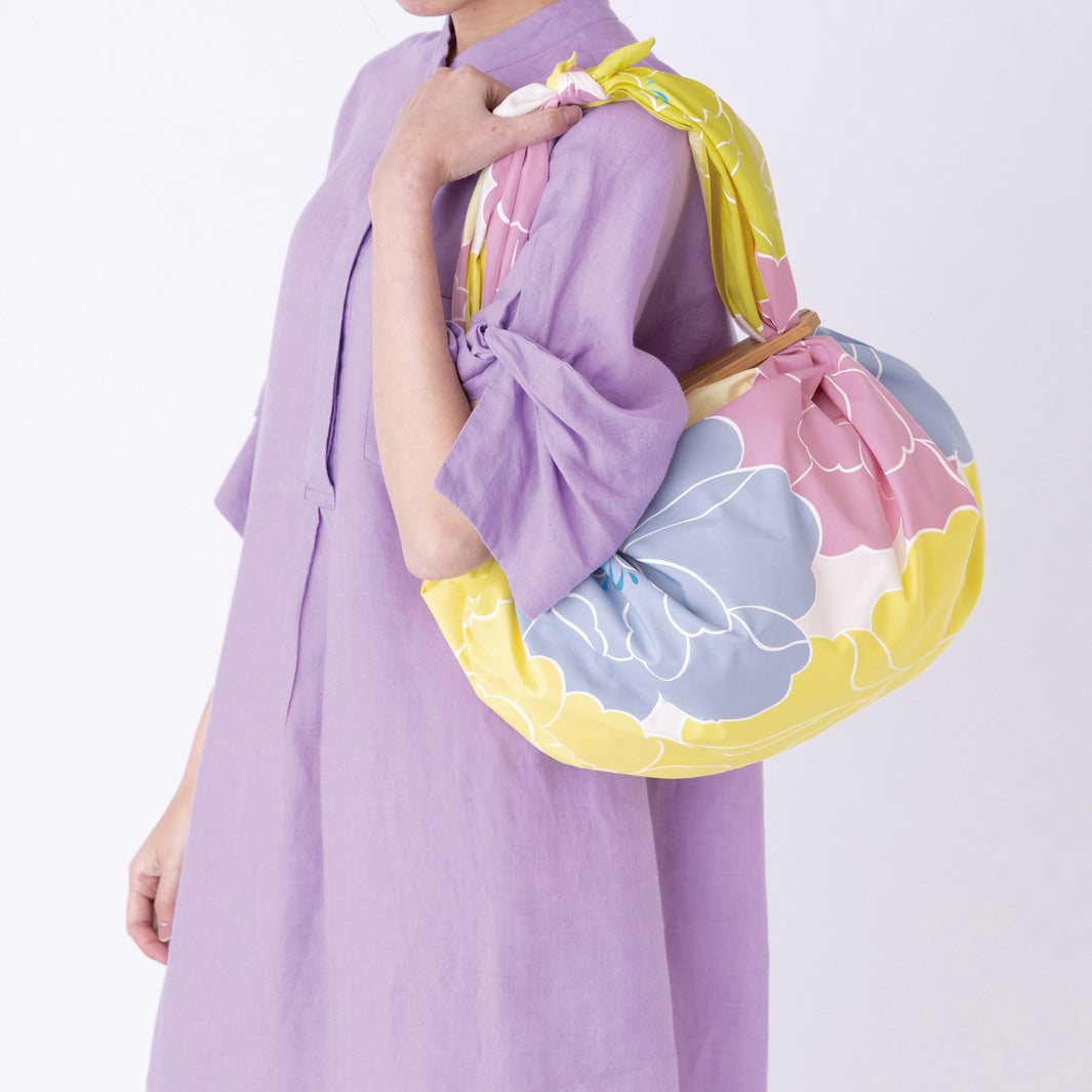photo d'ambiance d'un sac avec une anse réalisé avec le furoshiki au motif de pivoines dans les tons jaune pâle et acidulé, roses et bleu gris adeline x musubi en 100cm par 100cm