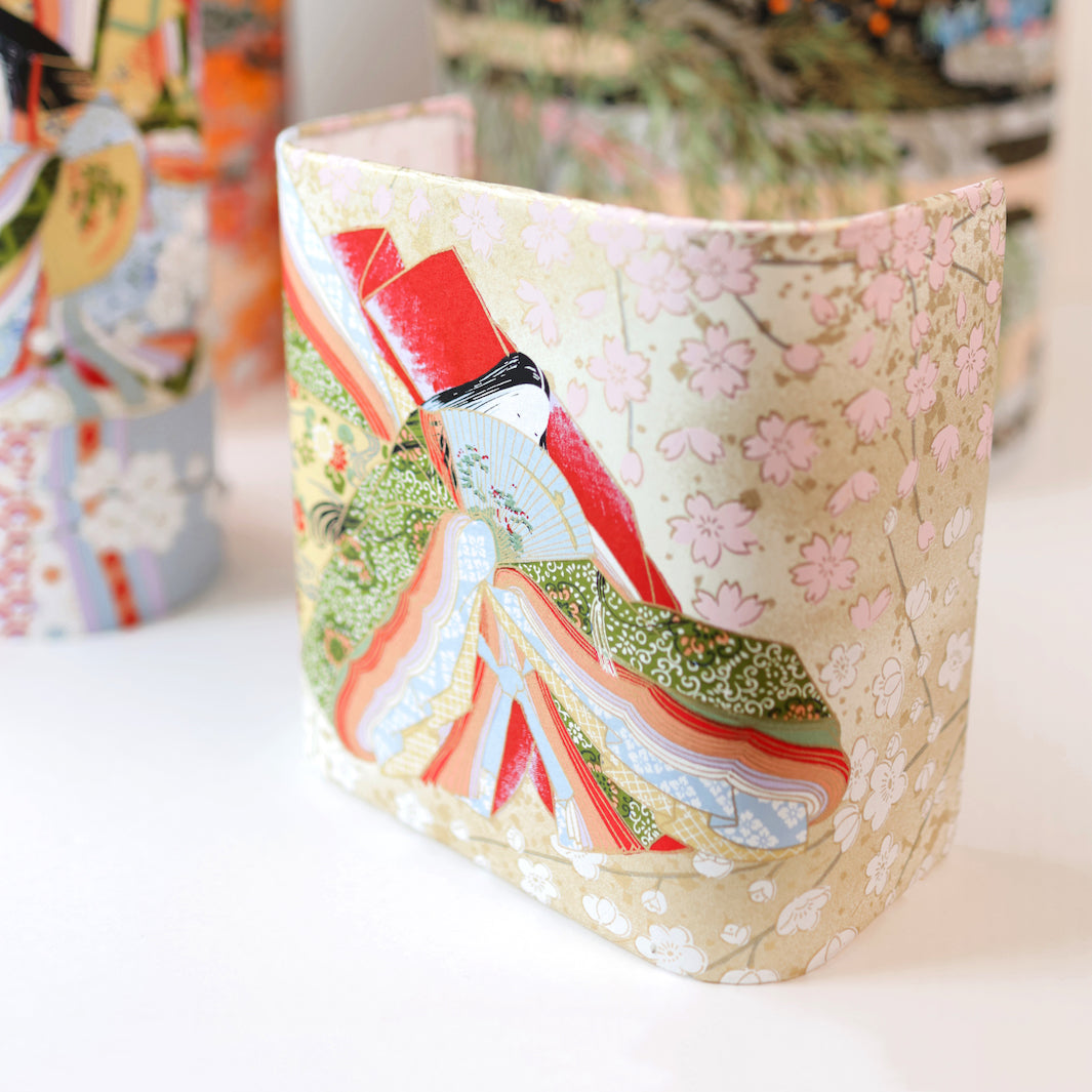 photo d'ambiance avec une vue de face en biais d'une applique murale japonaise au motif de femmes en kimono dans les tons mordorés, rouges, verts, bleus et mauves