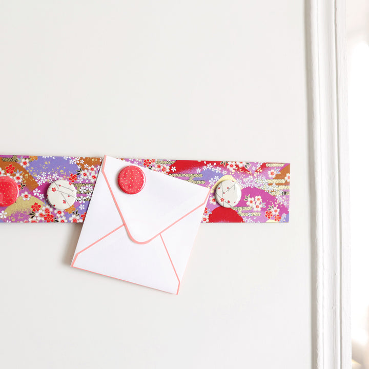 photo d'ambiance avec une vue zoomée du pêle-mêle tapissé du papier japonais aux motifs de fleurs, de montagnes et de nuages rouges, roses et violets M948 adeline klam