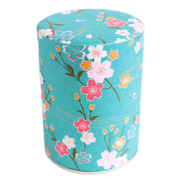 photo packshot d'une boîte à thé cylindrique fermée tapissée d'un papier japonais aux motifs de branches de fleurs de cerisier et d'ondulations dans les tons bleu turquoise, roses et dorés (M380) adeline klam