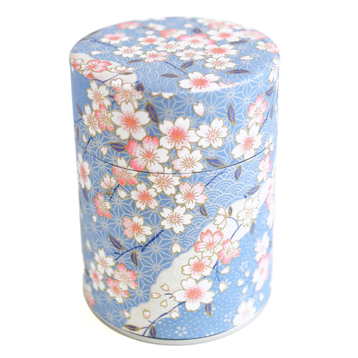 photo packshot d'une boîte à thé cylindrique fermée tapissée d'un papier japonais aux motifs de fleurs de cerisier, et de petits motifs japonais variés dans les tons bleu clair, roses et blancs (M384) adeline klam