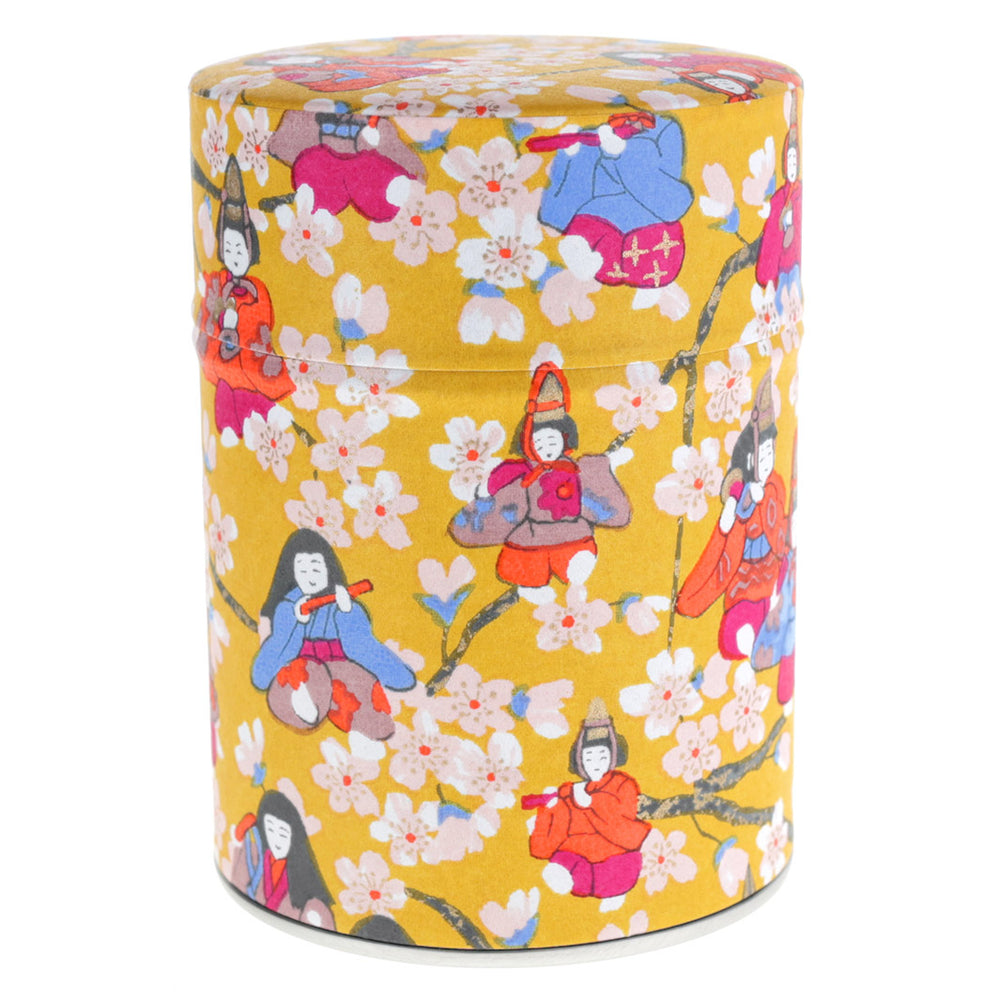 photo packshot d'une boîte à thé cylindrique fermée tapissée de papier japonais aux motifs de poupées d'hina matsuri et de fleurs de pêcher jaune moutarde, orange vif, rose fuschia, bleu clair et lie de vin (M1006) adeline klam