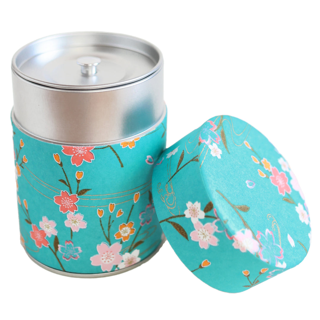 photo packshot d'une boîte à thé cylindrique ouverte tapissée d'un papier japonais aux motifs de branches de fleurs de cerisier et d'ondulations dans les tons bleu turquoise, roses et dorés (M380) adeline klam