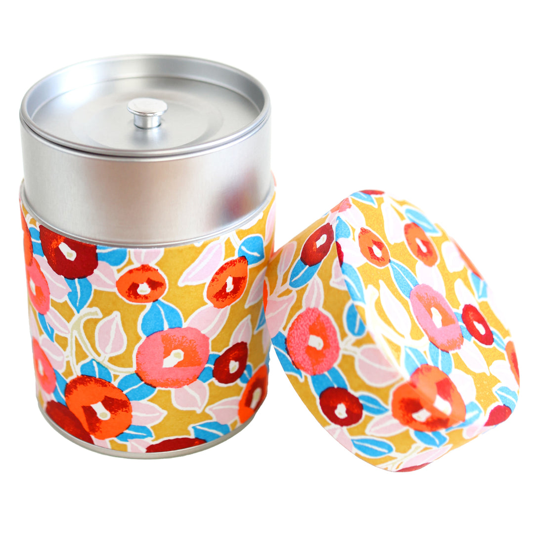 photo packshot d'une boîte à thé cylindrique ouverte tapissée d'un papier japonais aux motifs de camélias dans les tons jaune moutarde, rouges, roses et bleus (M802) adeline klam