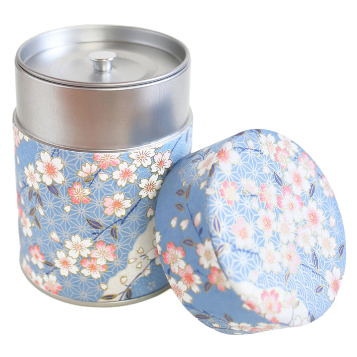 photo packshot d'une boîte à thé cylindrique ouverte tapissée d'un papier japonais aux motifs de fleurs de cerisier, et de petits motifs japonais variés dans les tons bleu clair, roses et blancs (M384) adeline klam