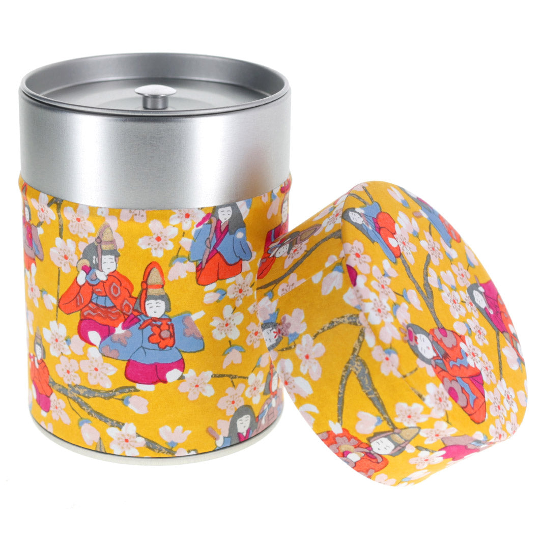 photo packshot d'une boîte à thé cylindrique ouverte tapissée de papier japonais aux motifs de poupées d'hina matsuri et de fleurs de pêcher jaune moutarde, orange vif, rose fuschia, bleu clair et lie de vin (M1006) adeline klam