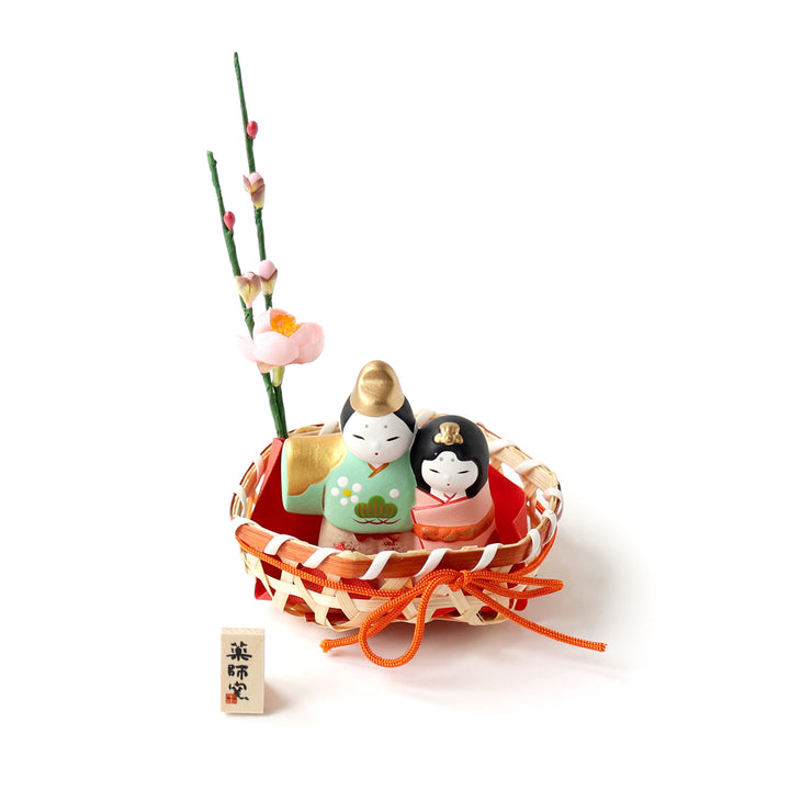 photo packshot du couple en céramique « hina matsuri » dans les tons vert d'eau, roses et dorés présenté dans son panier orné de fleurs de pêcher