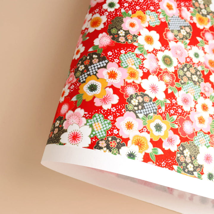 photo packshot d'une courbe de papier japonais yuzen chiyogami aux motifs de fleurs de cerisier traditionnelles blanches, roses, jaunes et vertes sur fond rouge adeline klam (M368)