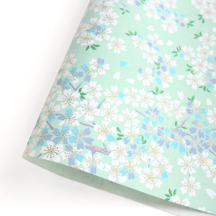 photo packshot d'une courbe de papier japonais yuzen chiyogami au motif de fleurs de cerisier blanches, bleues et mauves sur fond vert d'eau adeline klam (M626)