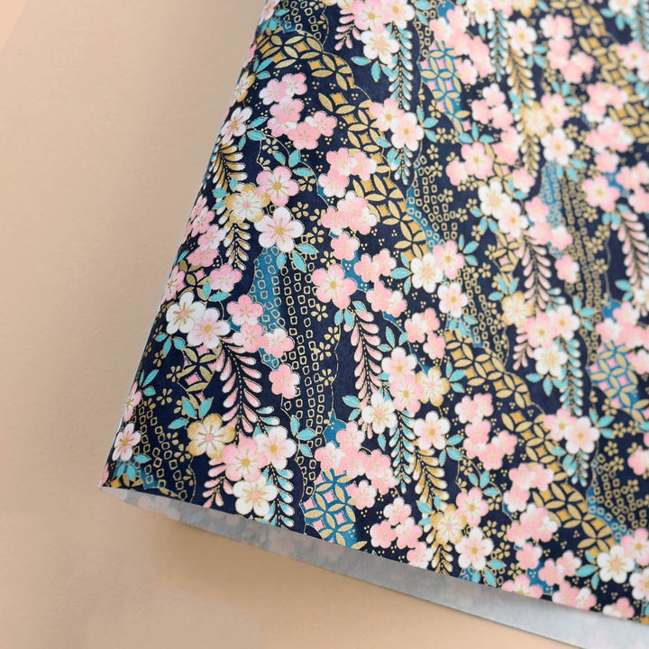 photo packshot d'une courbe de papier japonais yuzen chiyogami aux motifs de fleurs de prunier et de nuages à motifs dans les tons bleu marine et turquoise, jaunes, roses, blancs et dorés adeline klam (M1032)