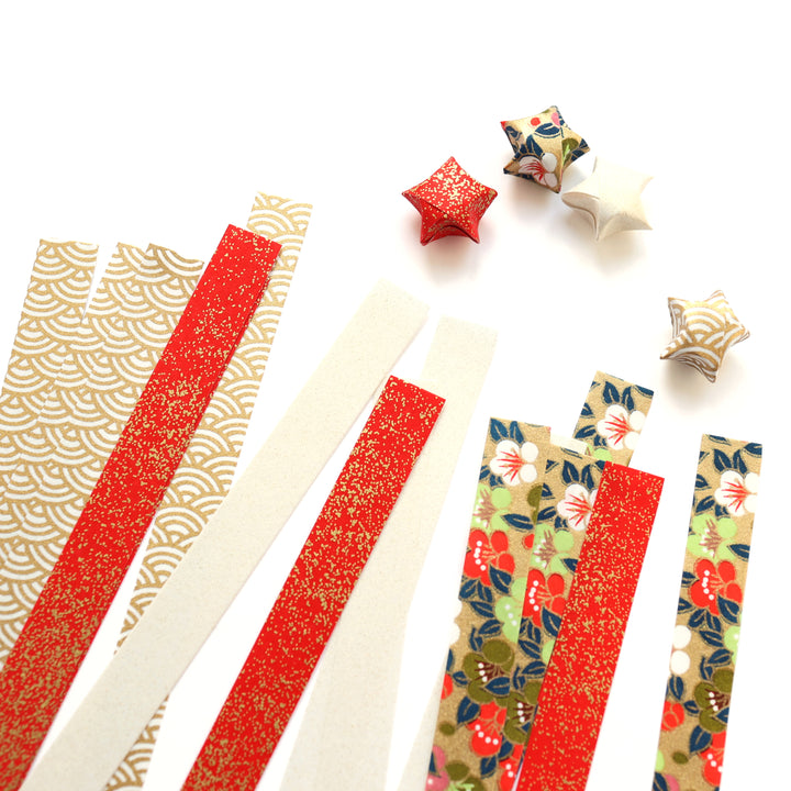 photo packshot des étoiles montées et des bandelettes de papiers japonais du kit étoiles en origami dans les tons dorés, rouges, blanc crème, verts et bleu foncé « festif » adeline klam
