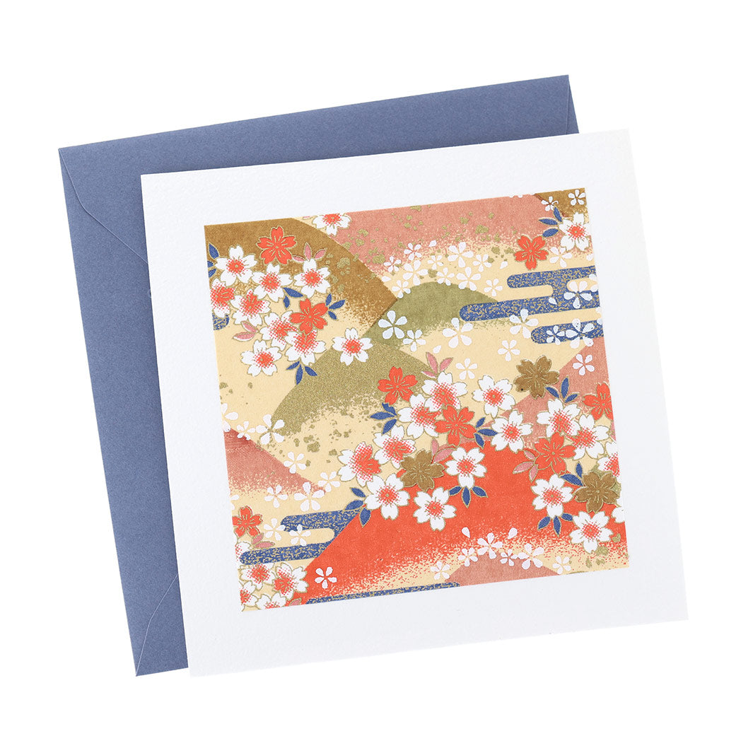photo packshot vue de face de la carte carrée double habillée d'un carré de papier japonais de 13cm au motifs de montagnes et de fleurs de cerisier dans les tons jaunes, orange, verts et bleus (M761) et son enveloppe bleu foncé adeline klam