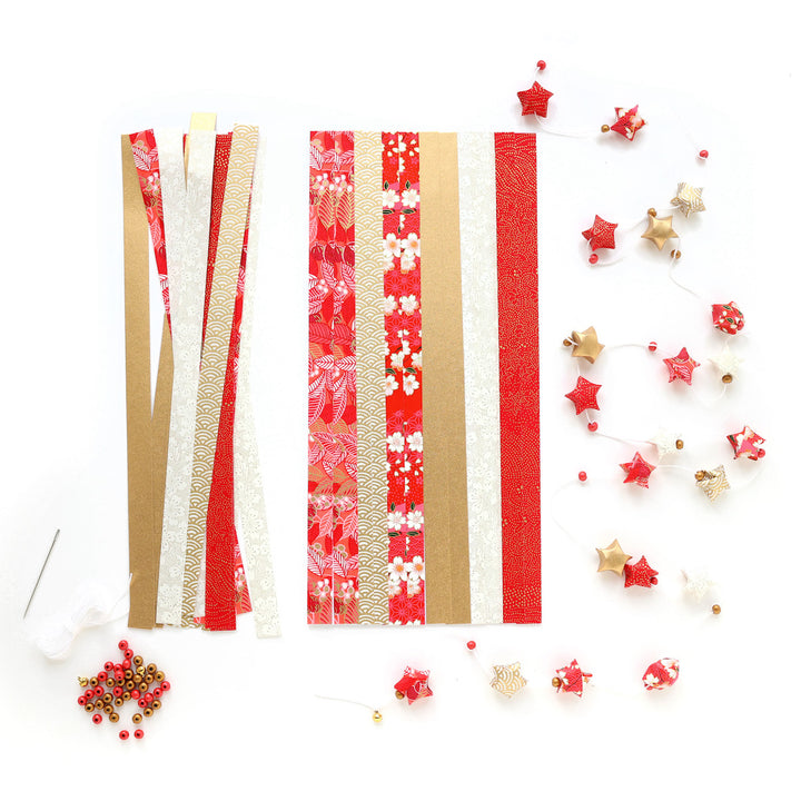 photo packshot de la guirlande montée et du matériel du kit guirlande d'étoiles en origami rouge, orange, rose corail, blanc cassé et doré « poinsettia » adeline klam