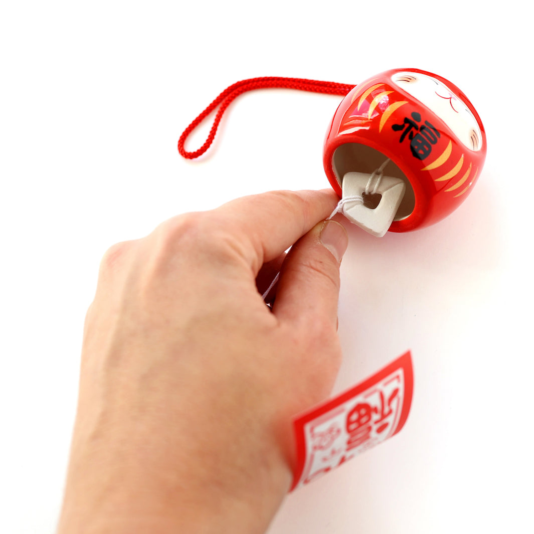 détail d'une clochette à vent japonaise en céramique rouge en forme de daruma chat